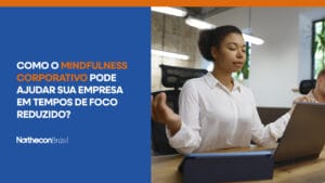 Mulher meditando no escritório, em frente ao computador, com o seguinte texto: Como o mindfulness corporativo pode ajudar sua empresa em tempos de foco reduzido?